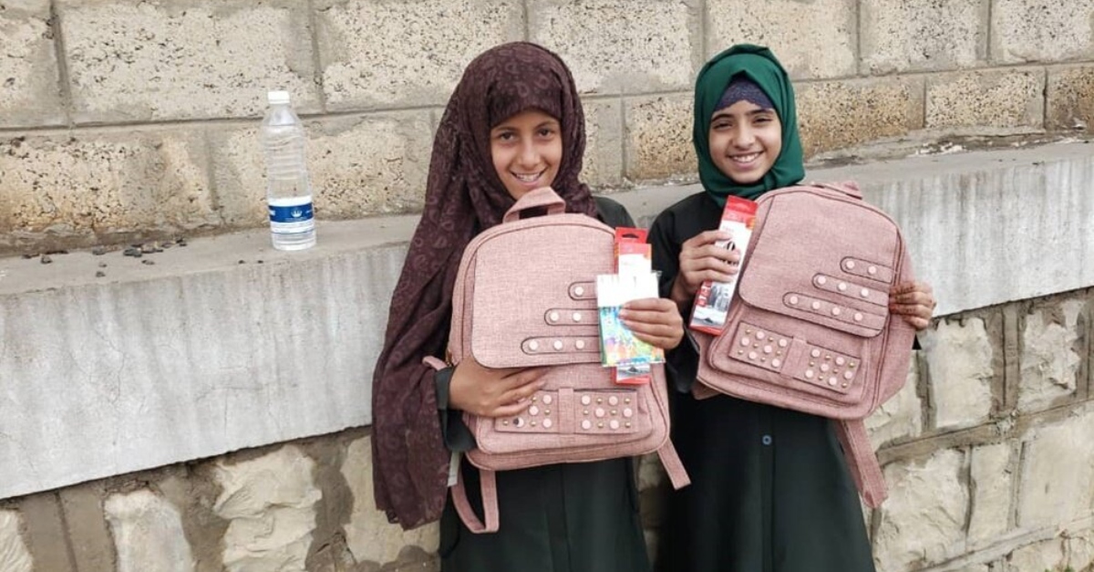 Two Yemeni girls stand with backpacks in front of schools at jeopardy of closing after the USAID fund cuts
