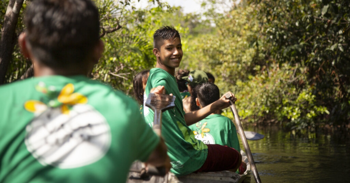 A young man looks to the person behind him on a canoe, smiling.