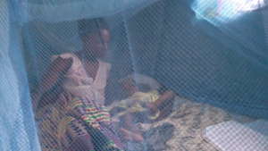 Beneficiary and baby under treated bed net.