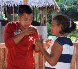 Jamner showing Romelia how to weave owl in Chino