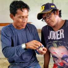 Pablo showing artisan how to weave blue jay