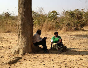 Mr Banda interviews a mother, shaded by a tree.