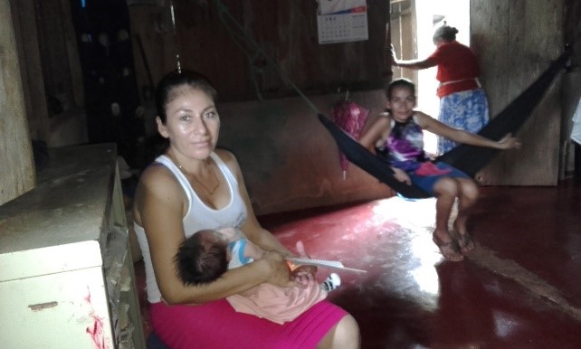 a woman nurses her child as she discusses clean water with SHI staff