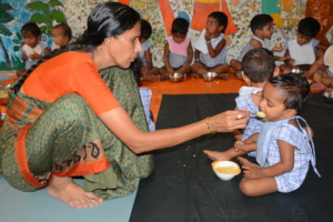 Teacher feeding nutritious meal to a creche child