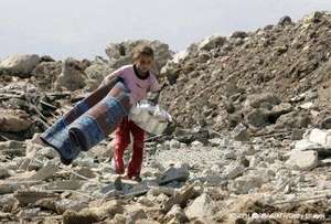 A girl walks over rubble with her belongings