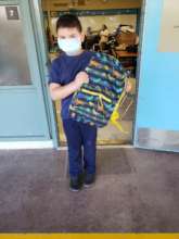 A little boy masked holding a colorful backpack