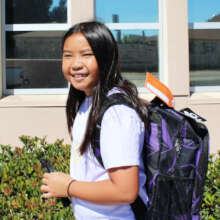 A smiling middle-schooler proudly wearing backpack