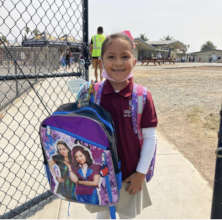 A lone girl smiling with her backpack in front