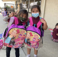 2 girls with their backpacks & making a peace sign