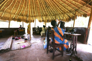 The women work in an outdoor thatched building.