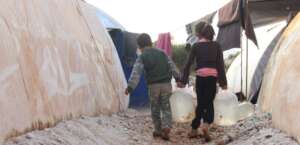 Children carry drinking water into their tents.