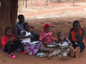 Kids eat a nutritious meal under the shade tree.