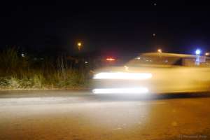 A sloth is hidden in the grass along a busy road