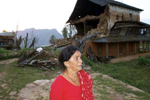 A Nepali woman walks past her badly damaged house