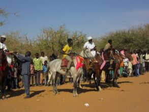 Some villagers greet him on horseback