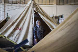 A woman stands outside her shelter in a camp