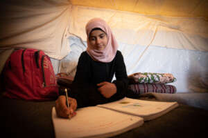 Basma does schoolwork in her family's tent.