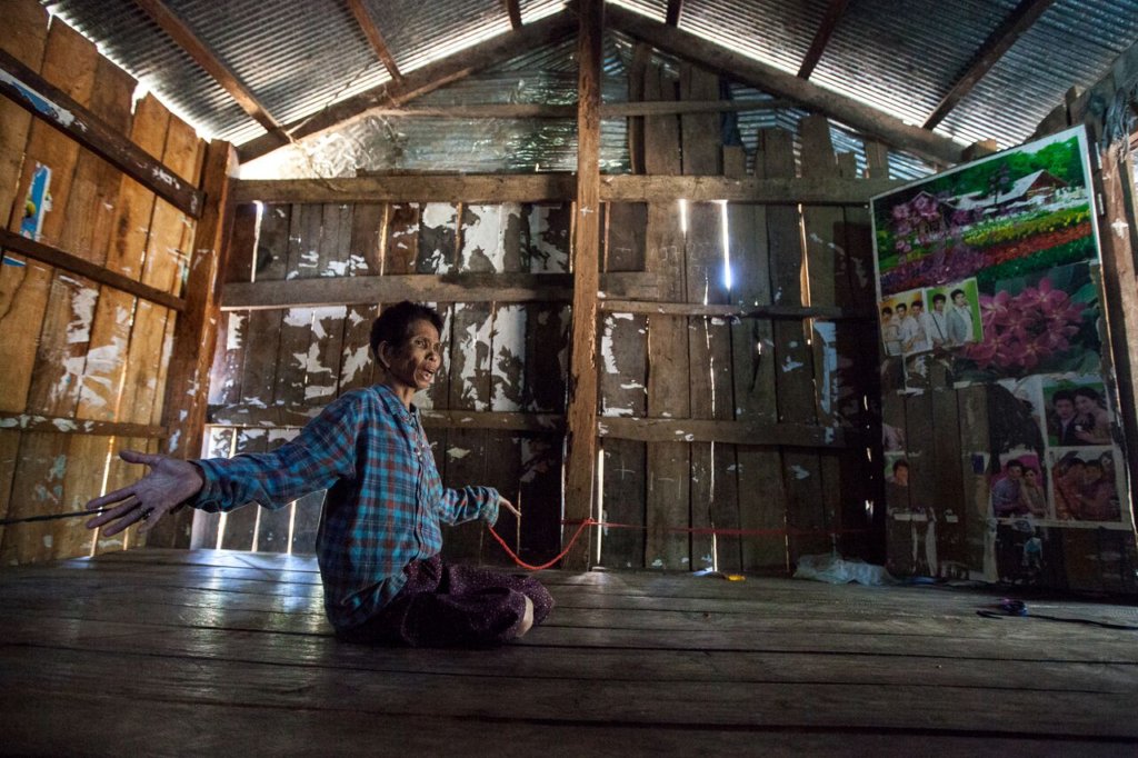 Patient is restrained by ropes to house's poles