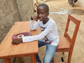 Gibril sitting at his table and chair
