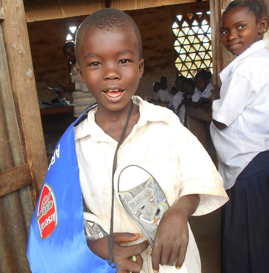 Hekima outside classroom with backpack & shoes