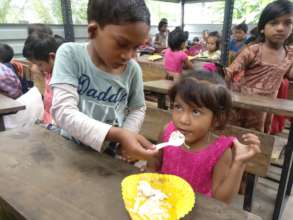 Mid-day meal: one tiny tot helping another