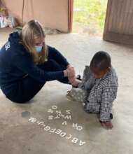A volunteer teaching alphabets to a NCP child