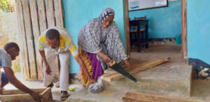 Mrs. Ali cutting a piece of wood to a good size