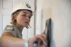 An AmeriCorps member repairs drywall for a home