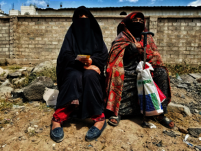 Mother, daughter sit outside a food distribution.