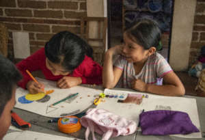 Hadasa draws next to her giggling sister Damaris