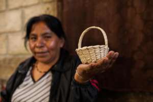 Salome teaches visitors to weave a small basket.