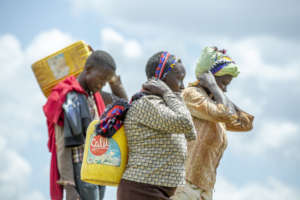 Walking with water buckets strapped to their backs