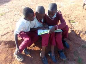 Pupils helping each other read outside the school