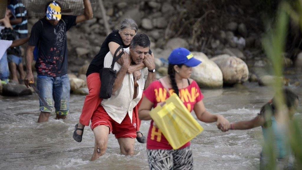 SAI Volunteer carries migrant woman on his back.