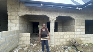Ruth stands in front of her unfinished home.