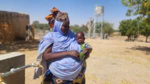 Woman and baby with water tank in background