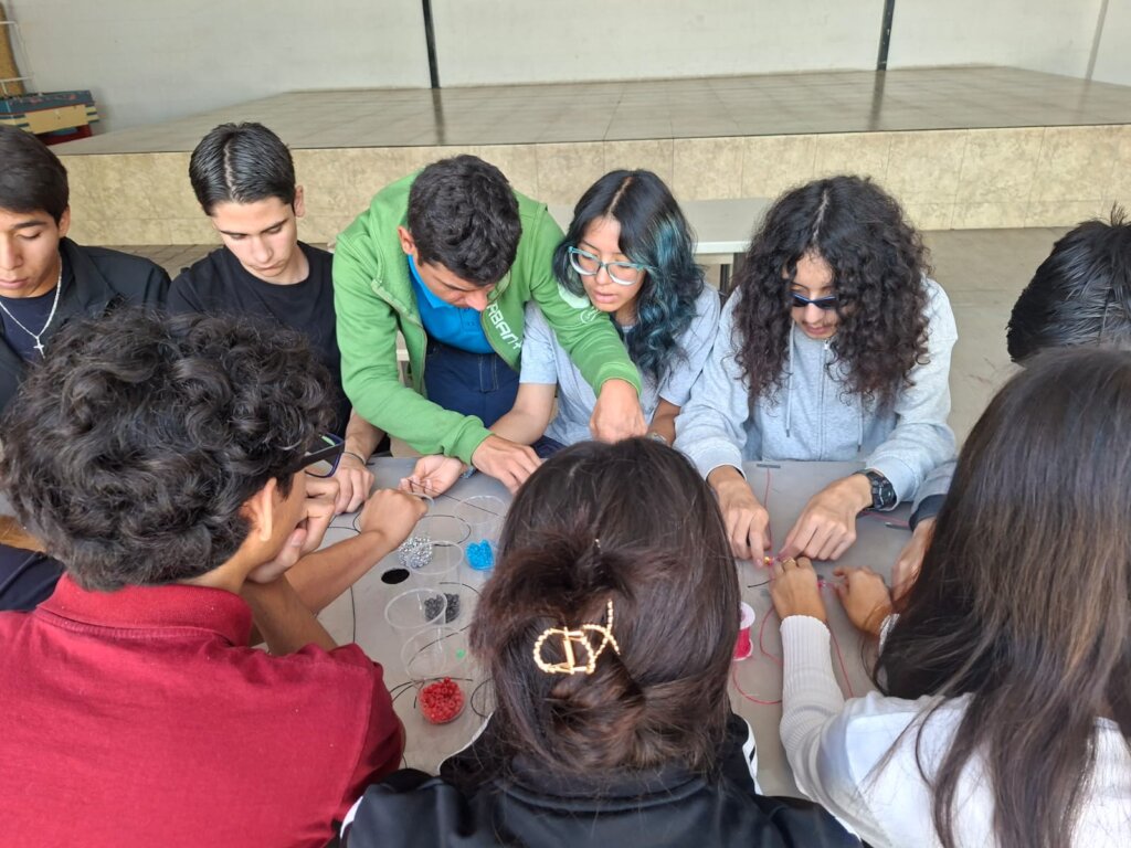 Alex (green hoodie) teaching HS students bead work