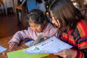 The teacher supporting the girl in reading