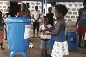 Little girl washes her hands at a Maji Bucket
