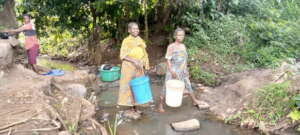 Joice, with white bucket, crossing the river.