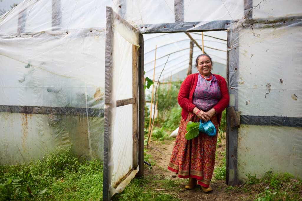 A happy woman standing by her greenhouse