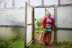 A happy woman standing by her greenhouse
