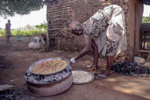 Refugee woman bakes mandazi biscuits over charcoal