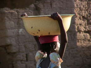 Young girl carries heavy basin of water.