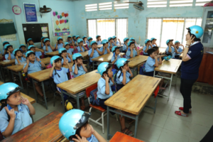 A volunteer teaches students how to wear helmets.