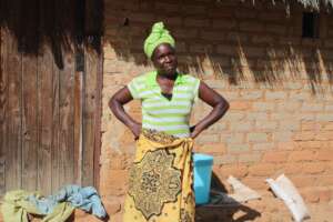 Faith in front of her thatched hut...