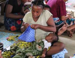 Woman making a reusable pad while holding her baby