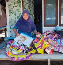 Ibu W in front of her home, with some new bags
