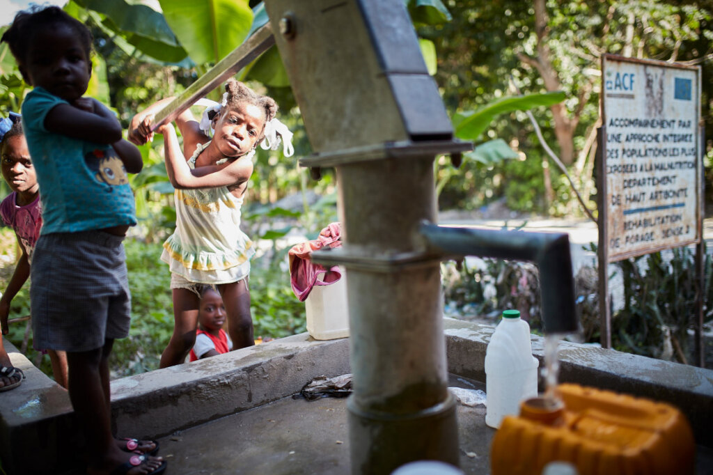 A young girl pumps water from a pump built by AAH