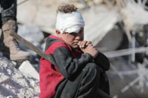 Ward*, 6, sits in rubble near his destroyed home.